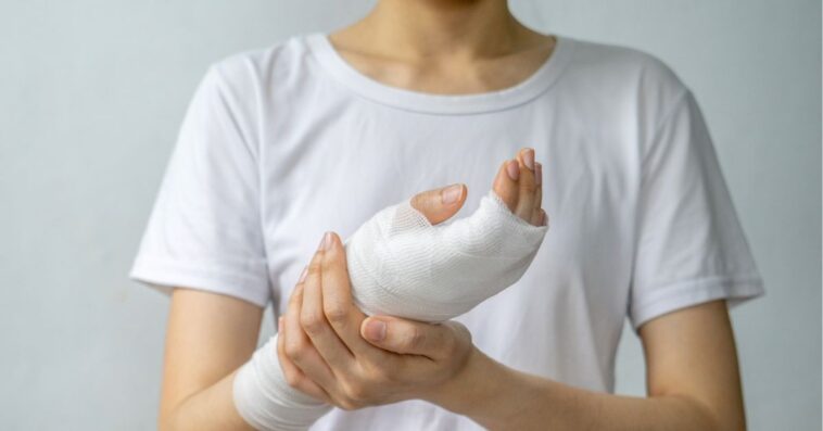 A young woman holds up her bandaged hand.