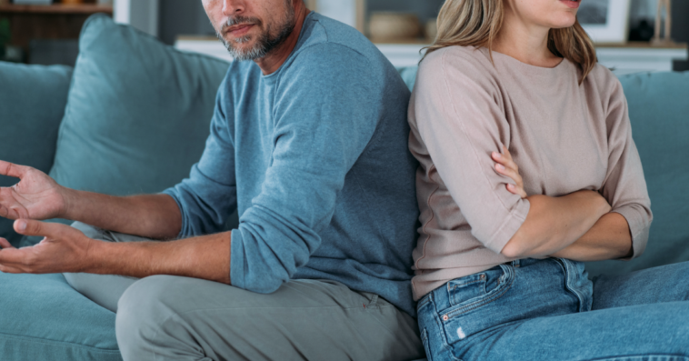 A couple sitting on a sofa facing away from one another.