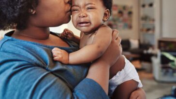 Shot of a woman holding and kissing the head of a crying baby.