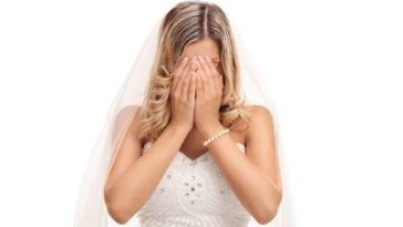 A young bride cries into her hands, she is isolated against a white background.