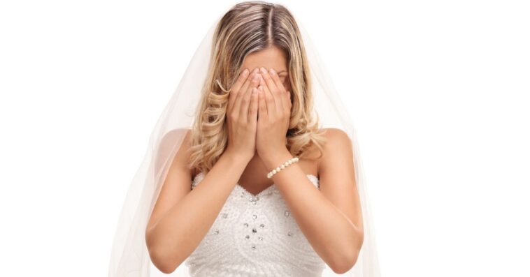 A young bride cries into her hands, she is isolated against a white background.