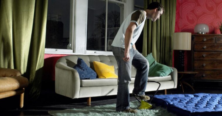 Young man using foot pump on air mattress in living room.