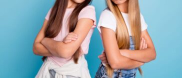 Two frowning adolescent girls stand back to back with their arms folded.
