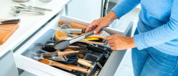 Unrecognizable woman organizing a messy kitchen drawer with a lot of kitchen utensils.