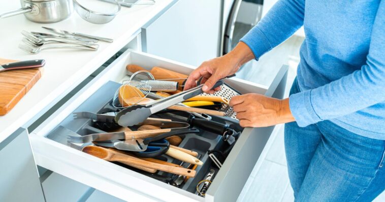 Unrecognizable woman organizing a messy kitchen drawer with a lot of kitchen utensils.
