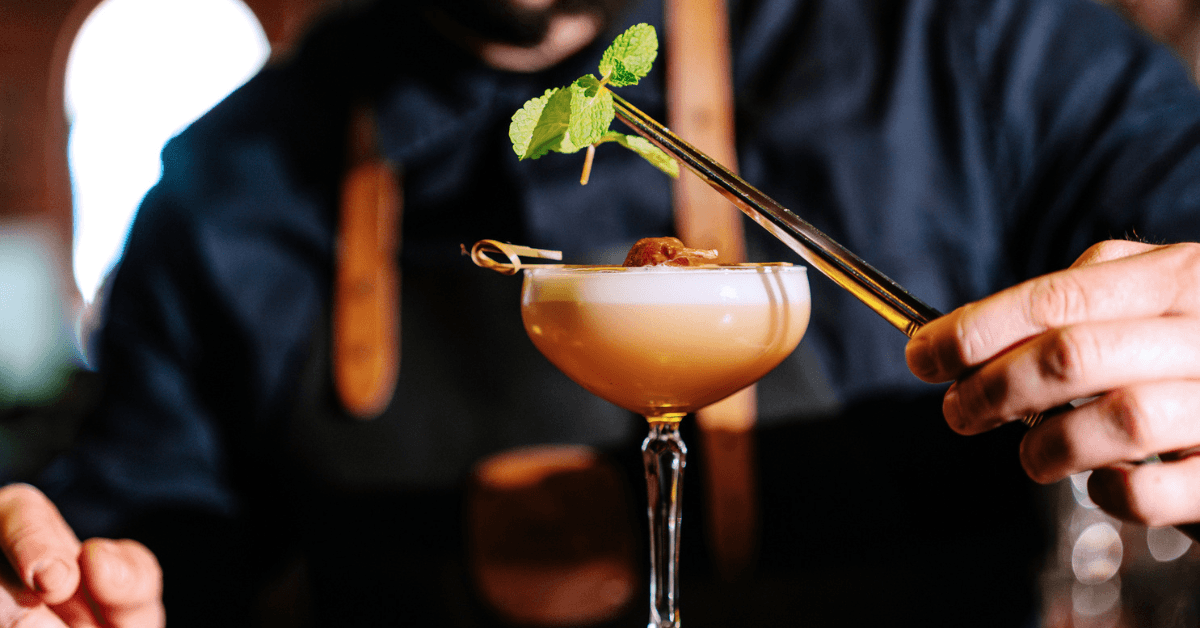 A putting a leafy garnish over a frothy cocktail.