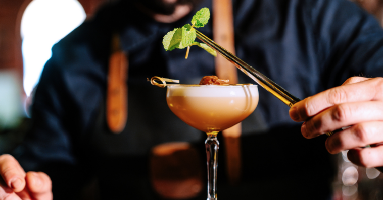 A putting a leafy garnish over a frothy cocktail.