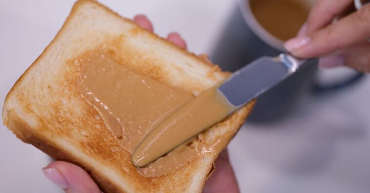Woman spreading peanut butter on toast closeup. Quick breakfast concept