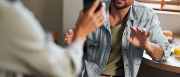 Worried man explaining himself to his girlfriend who found some suspicious text messages on his cell phone.