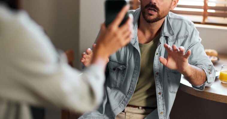 Worried man explaining himself to his girlfriend who found some suspicious text messages on his cell phone.