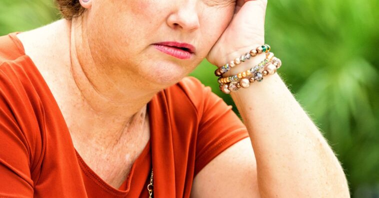 A concerned, serious, mature redhead woman stares off in space.