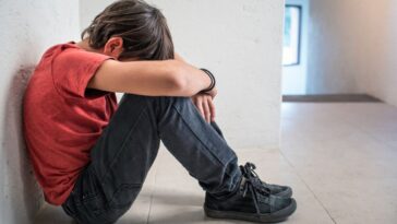 A depressed, sad, upset boy sitting on floor with his head down.