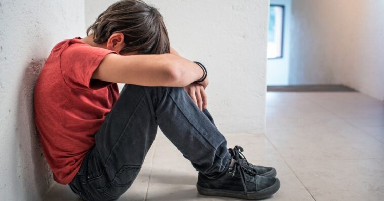 A depressed, sad, upset boy sitting on floor with his head down.