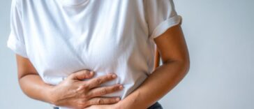 Mid-shot of a woman holding her stomach, crippled by pain.