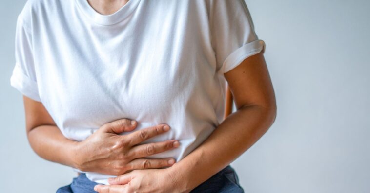 Mid-shot of a woman holding her stomach, crippled by pain.