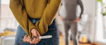 Woman holding a positive pregnancy test behind her back