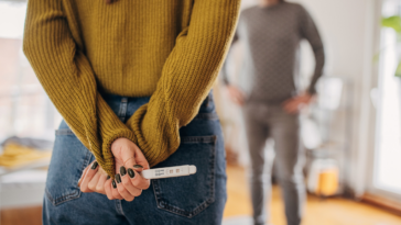 Woman holding a positive pregnancy test behind her back