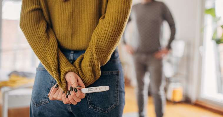 Woman holding a positive pregnancy test behind her back