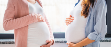 Two pregnant women patting their pregnant stomachs.