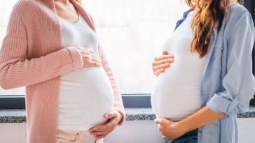 Two pregnant women patting their pregnant stomachs.