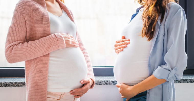 Two pregnant women patting their pregnant stomachs.