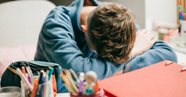 A teenage boy resting his head on a desk.
