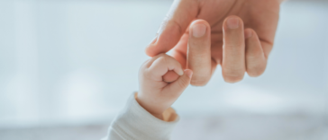 A baby holding a grown ups hand