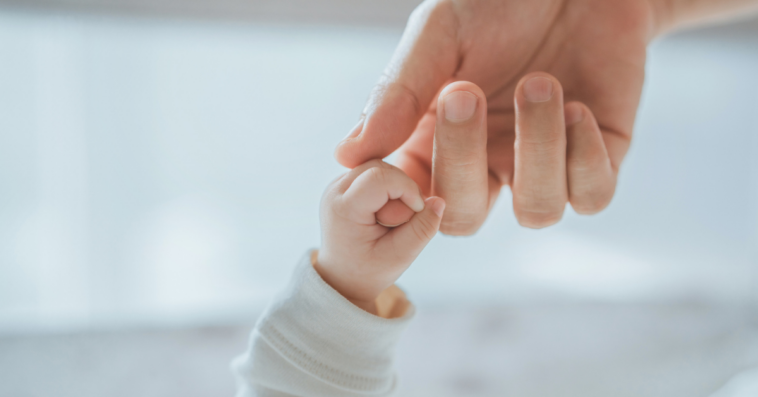 A baby holding a grown ups hand