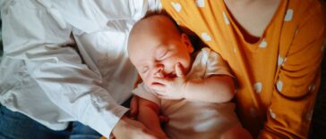 Mom with newborn baby and daughter in a cozy real home, genuine moments of motherhood. Mom embraces both children.