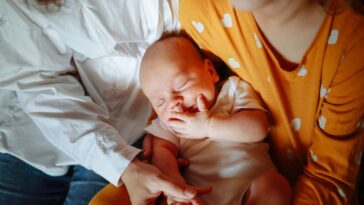 Mom with newborn baby and daughter in a cozy real home, genuine moments of motherhood. Mom embraces both children.