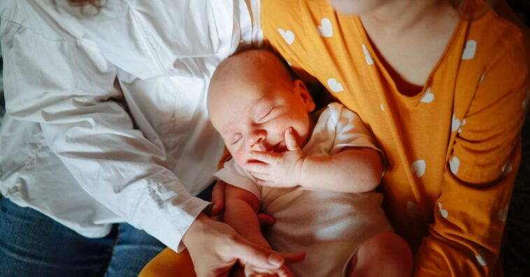 Mom with newborn baby and daughter in a cozy real home, genuine moments of motherhood. Mom embraces both children.