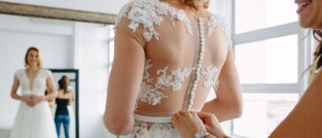 A bride with a dressmaker are making final touch on tailor made gown in bridal clothing shop.