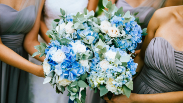 Three bridesmaids in gray, strapless bridesmaid's dresses surrounding a bride holding bouquets.