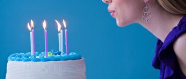 Young woman blowing out candles on a birthday cake, studio shot, light blue background.