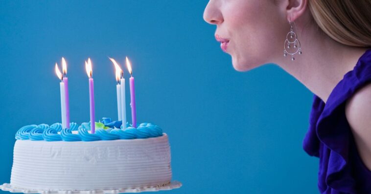 Young woman blowing out candles on a birthday cake, studio shot, light blue background.
