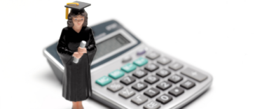 A figurine in a graduation cap and gown placed in front of a calculator.