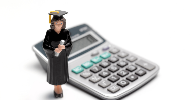A figurine in a graduation cap and gown placed in front of a calculator.