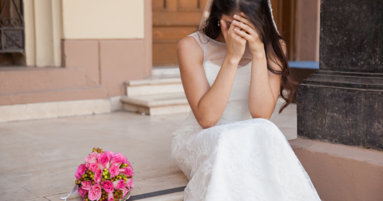 A bride sitting on steps crying into her hands.