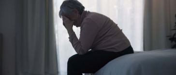 A woman sitting on a bed with her head in her hands.
