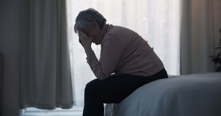 A woman sitting on a bed with her head in her hands.