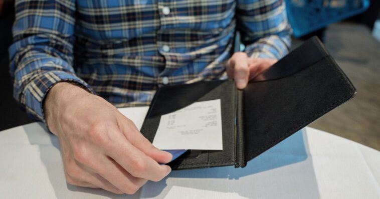 Close-up of unrecognizable man reviewing check at restaurant while placing credit card in holder.