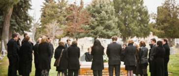 A group of people around a coffin in a graveyard.