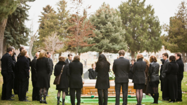 A group of people around a coffin in a graveyard.