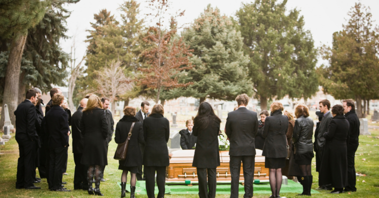 A group of people around a coffin in a graveyard.