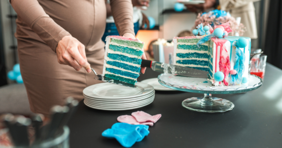 A pregnant woman cutting into a blue gender reveal cake.