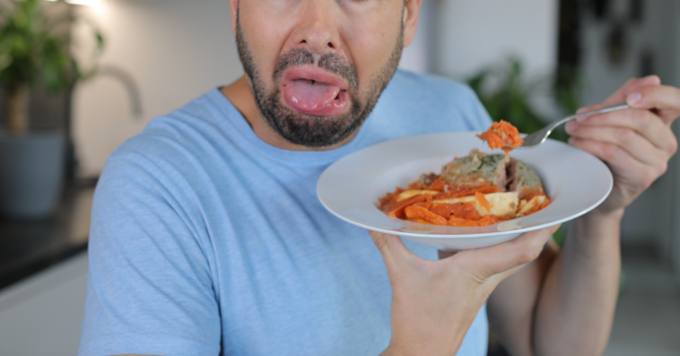 A man holding a plate of food with a grossed out expression on his face.