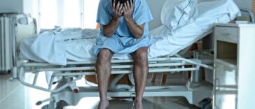 A sad, sick man sits on a hospital bed alone and depressed.