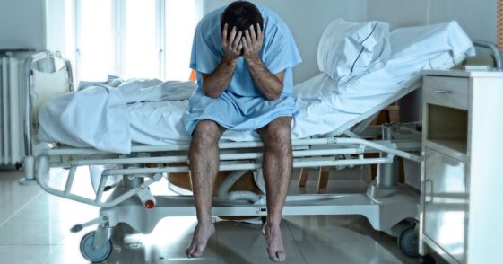 A sad, sick man sits on a hospital bed alone and depressed.