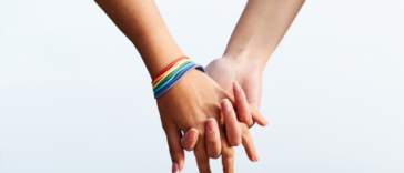 two women's clasped hands with rainbow bracelet