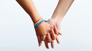 two women's clasped hands with rainbow bracelet
